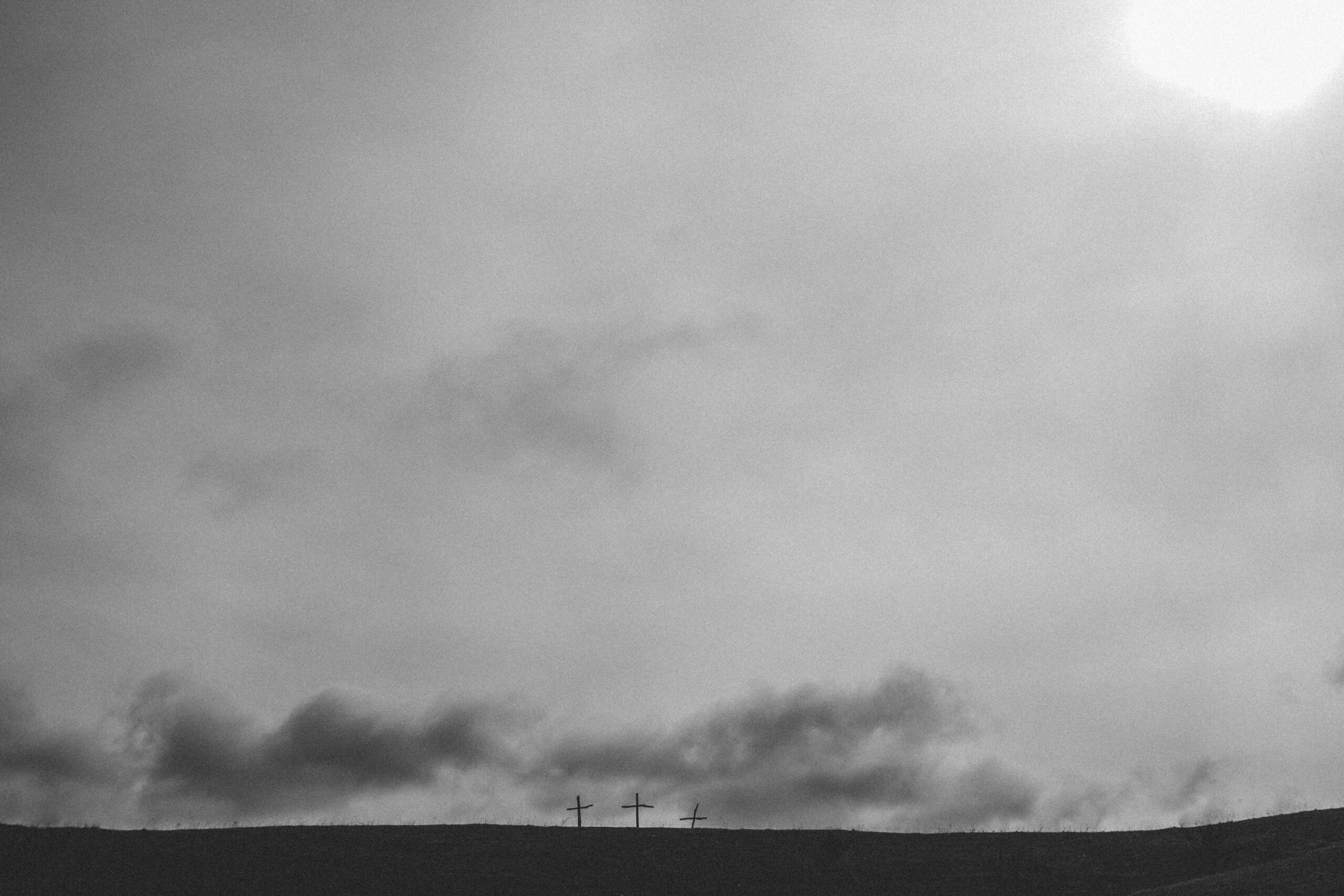 Three wooden crosses on a grey hill with a grey sky.
