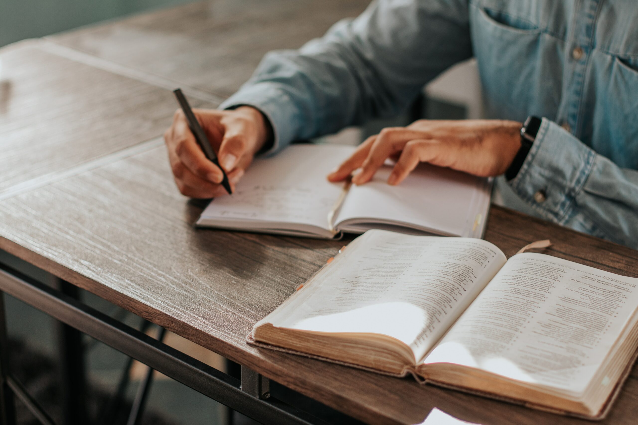 Man writing in a notebook while studying the Bible.